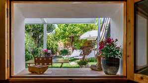 A view through a wooden-framed window into a patio area with a table, chairs, a bench, and a potted plant.