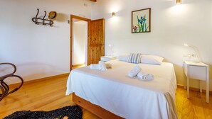A bedroom with a wooden bed, white linens, a painting, a nightstand, and a door.