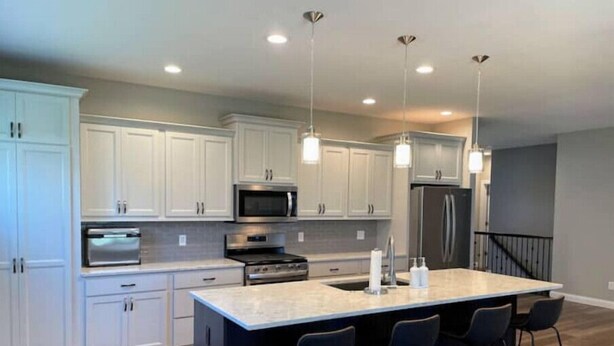 Una cocina moderna con armarios blancos, electrodomésticos de acero inoxidable, una isla grande con taburetes de bar e iluminación colgante.