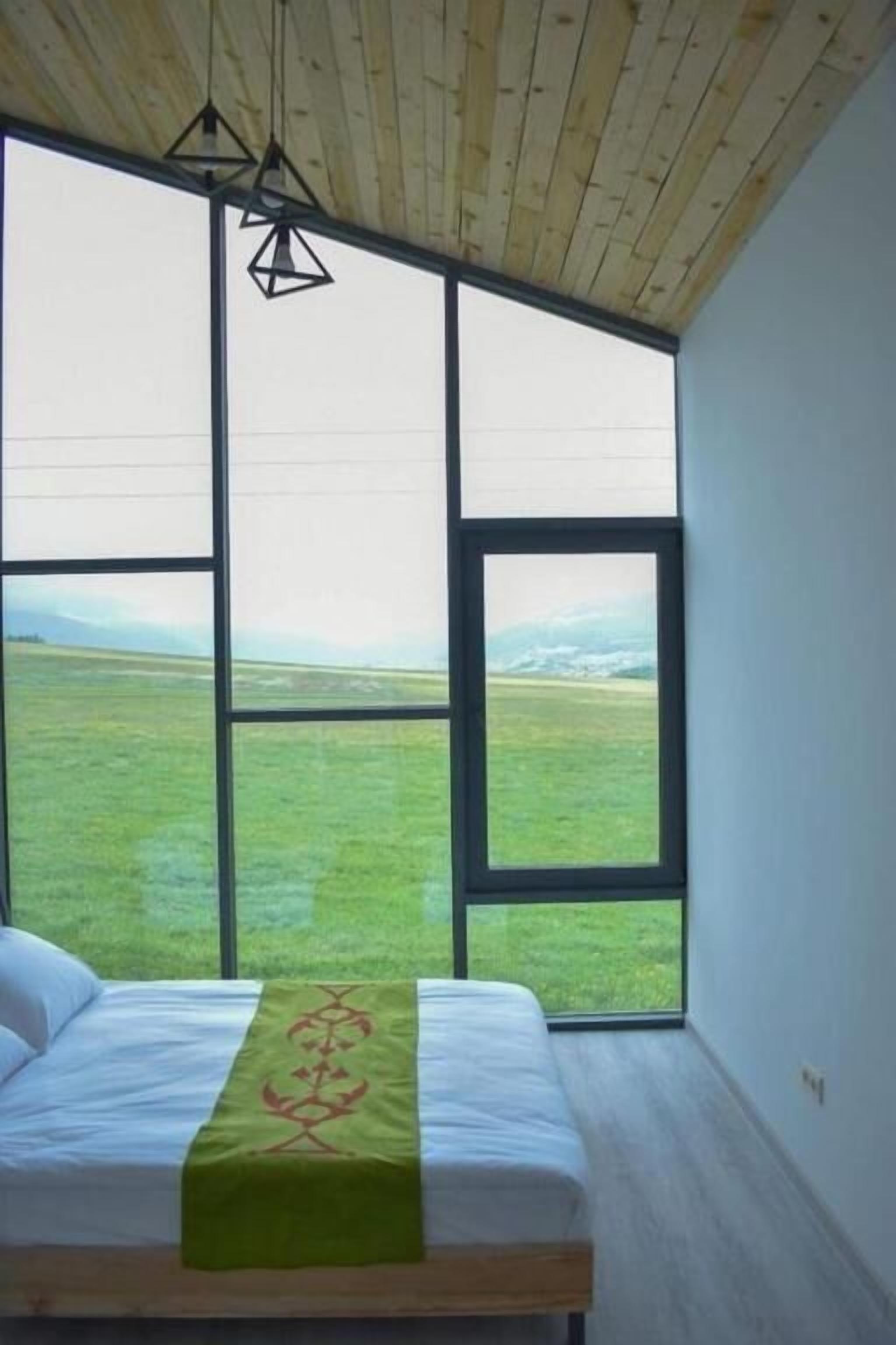 Un dormitorio con un ventanal grande, una cama y una lámpara colgante.