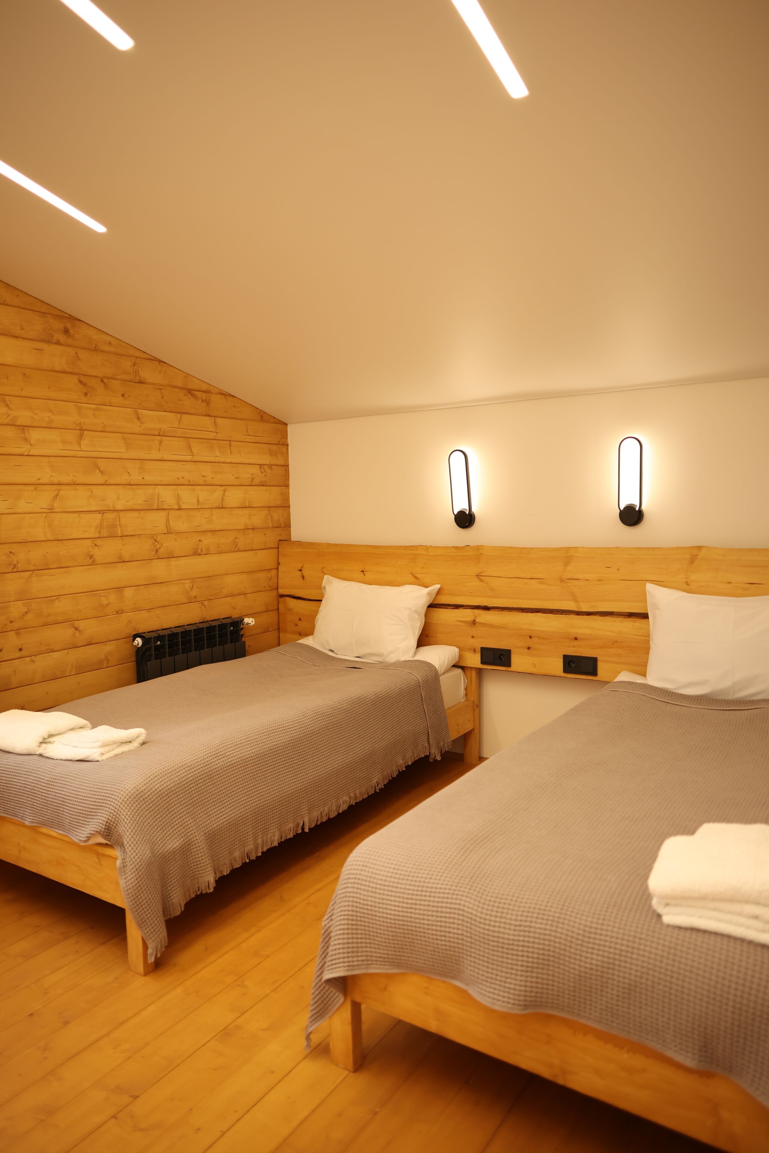 A room with two wooden beds, a radiator, and wall-mounted lighting.