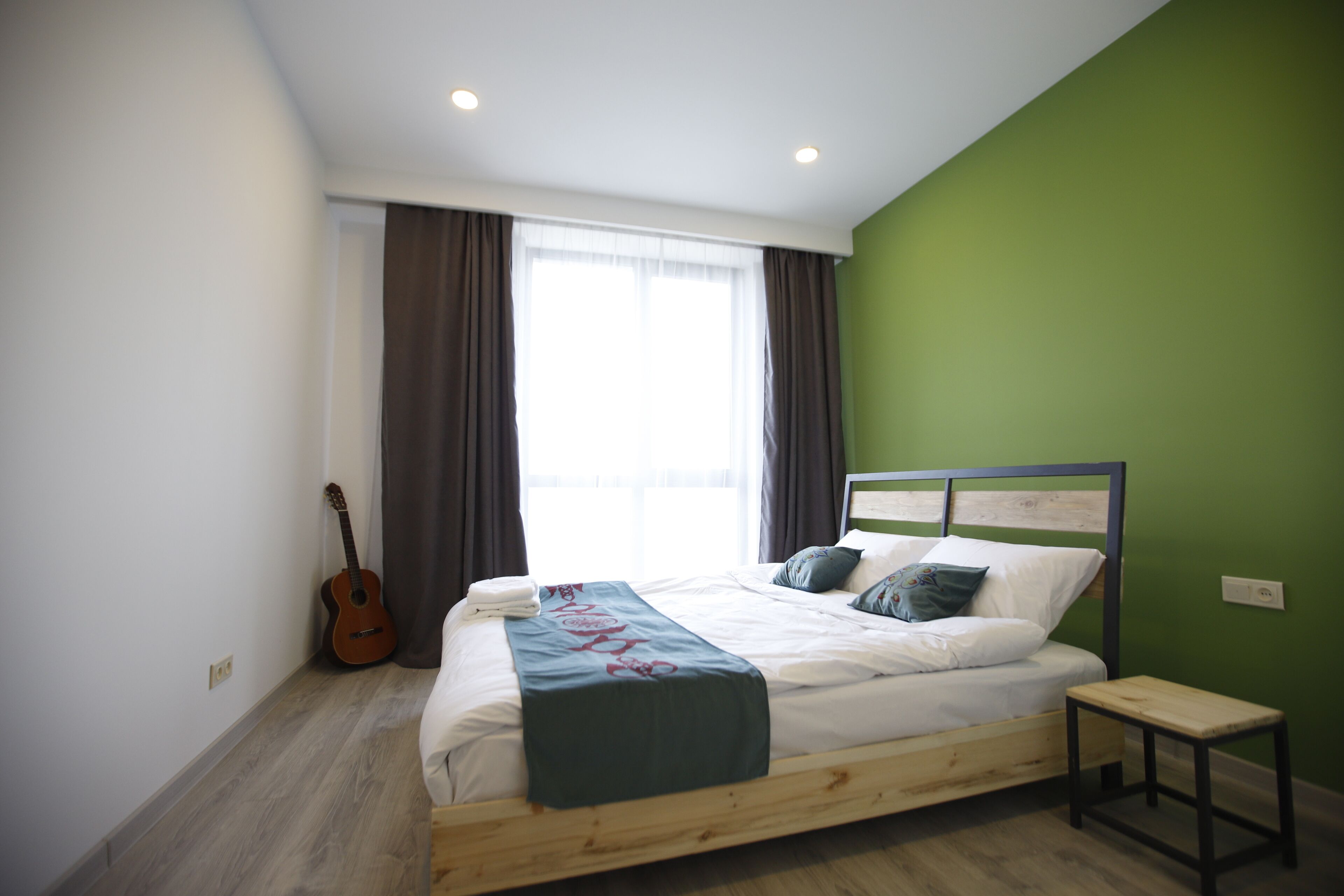 Quarto com cama, um violão, um banco e janela com cortinas.