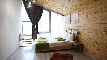 A bedroom with a wooden ceiling, a bed with pillows, a bench, and a window with curtains.