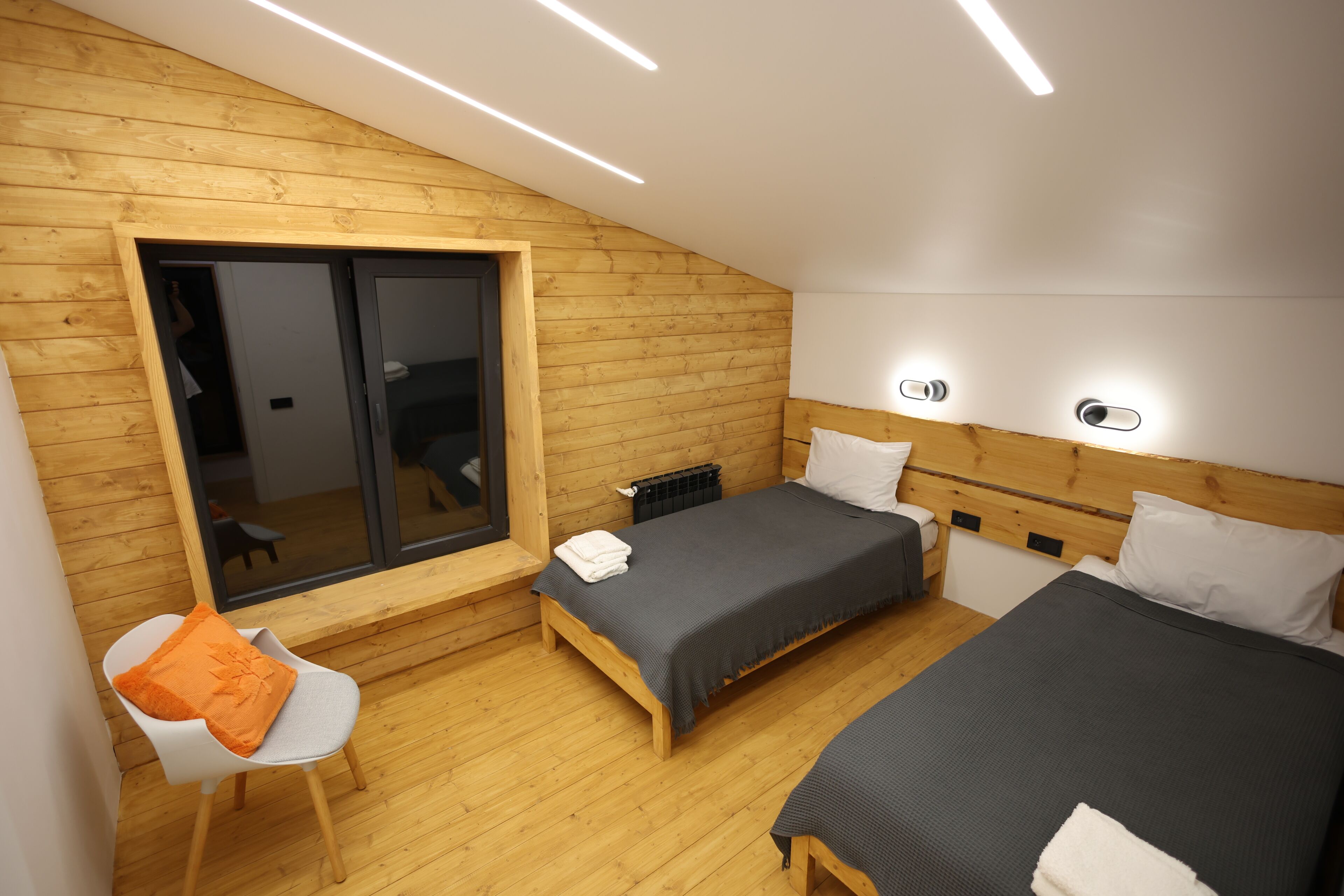 A modern bedroom with wooden walls, two beds, a bench, and a sliding door.