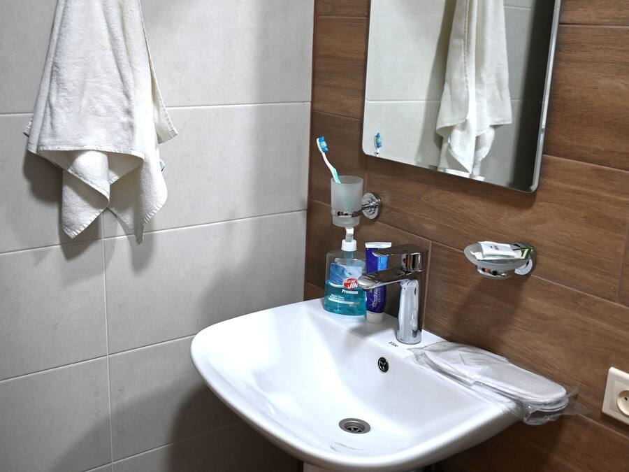 Ein Badezimmer mit einem weißen Waschbecken, einem Spiegel und einem Handtuch, das an der Wand hängt.
