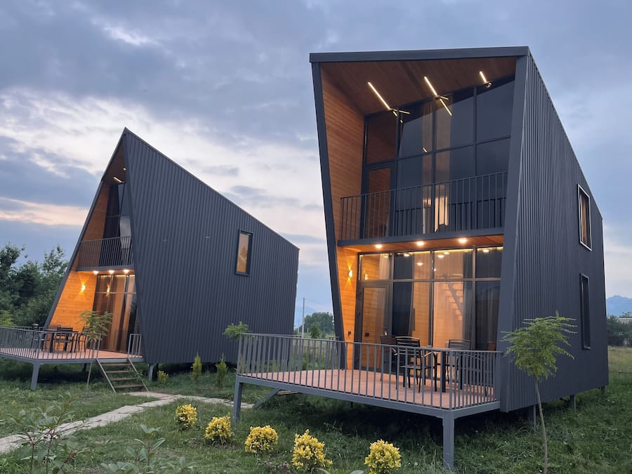 Two modern, dark-colored buildings with balconies, wooden deck areas, and outdoor seating.