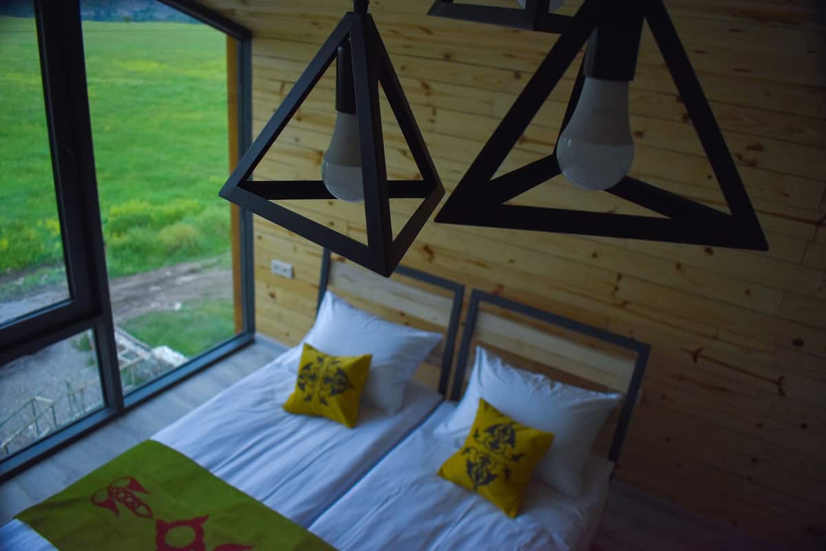 Una habitación con dos camas, paredes de madera y una ventana con vista a un campo verde.