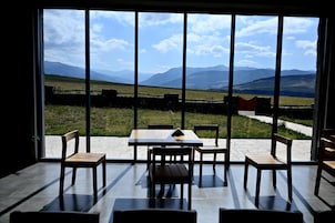 Comedor con vista a un campo verde y montañas a través de amplios ventanales.