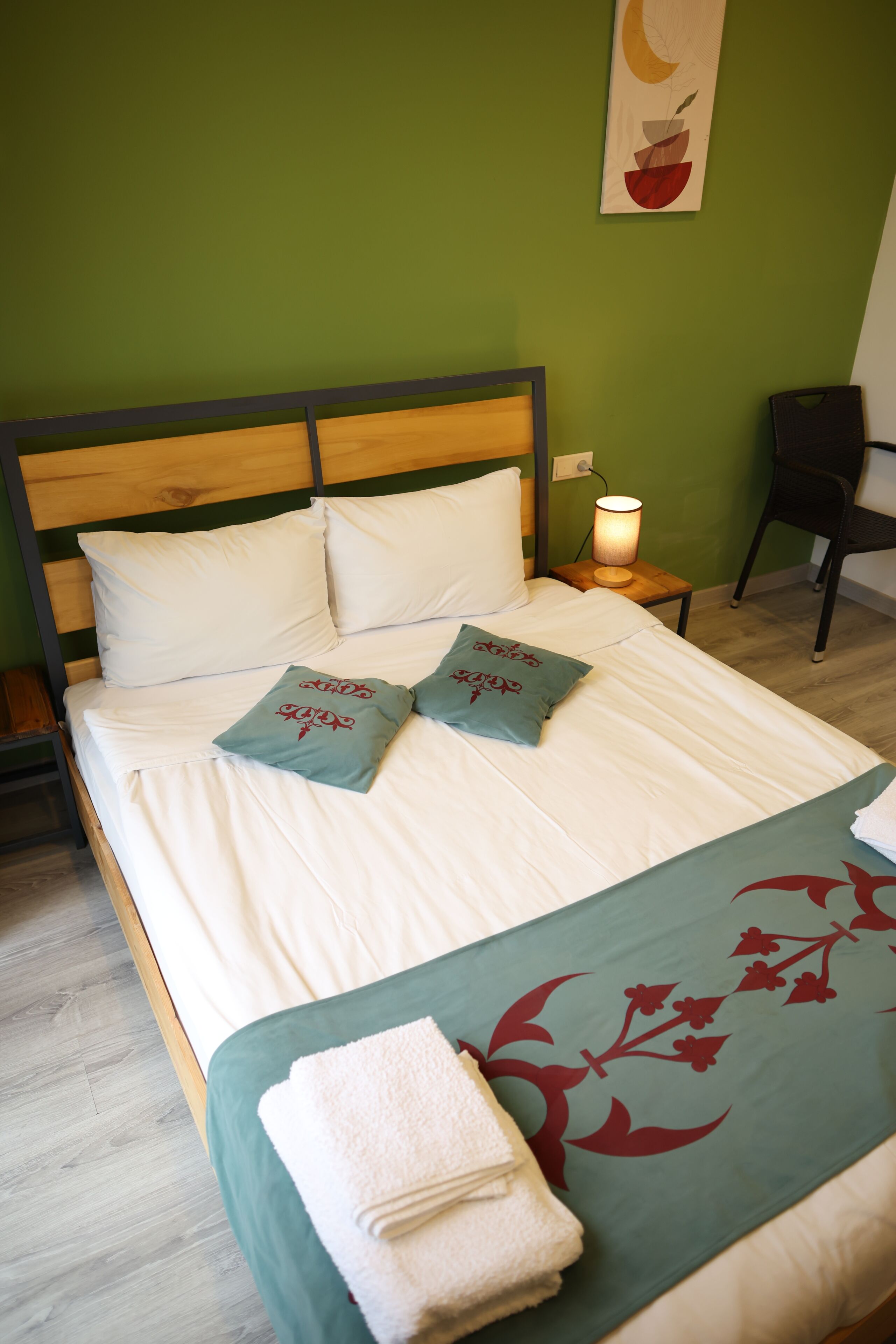 A neatly made bed with white bedding and decorative pillows, a bedside lamp, and a chair in a room with green walls.