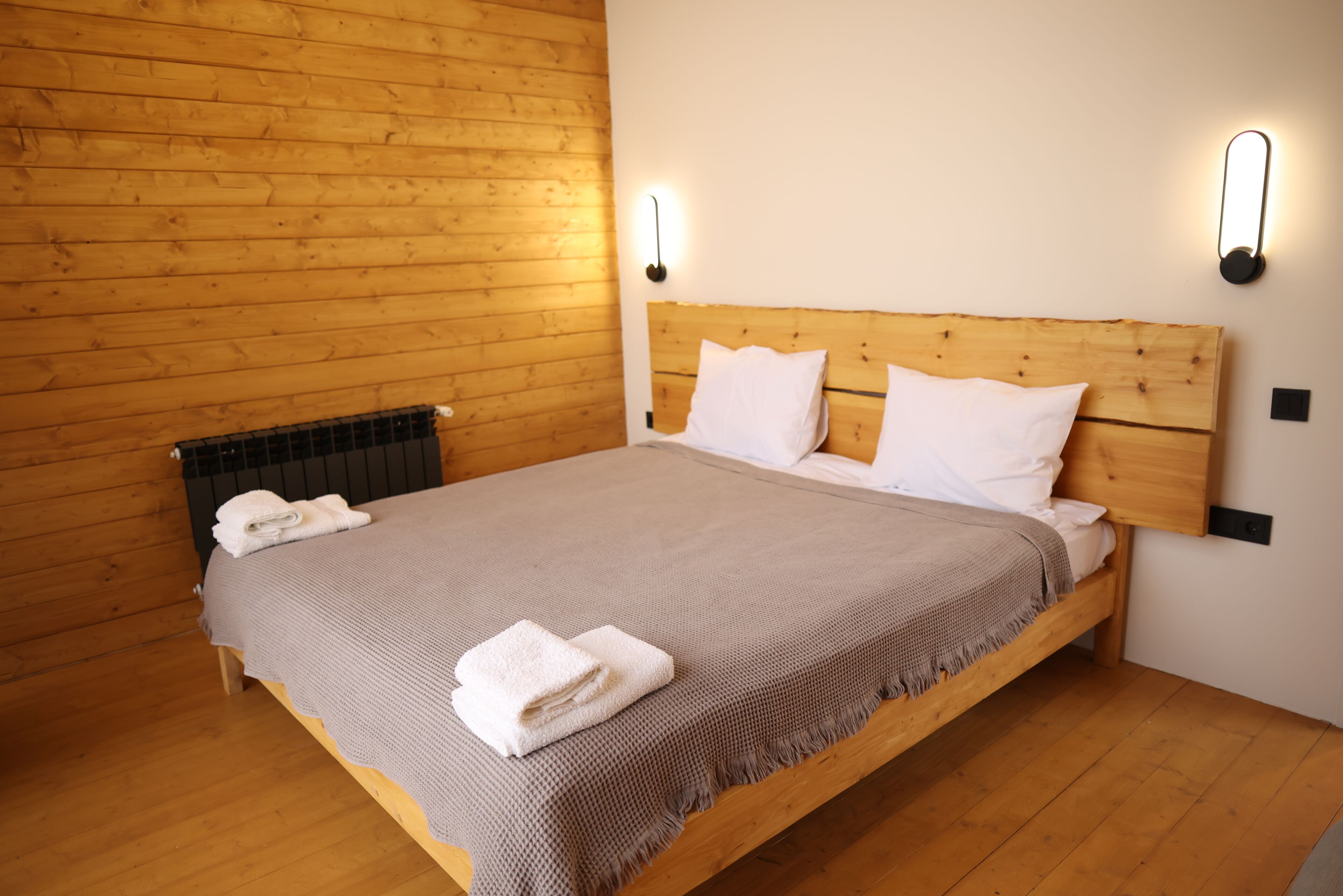 Un lit simple avec une tête de lit en bois, des oreillers blancs et une couverture grise.