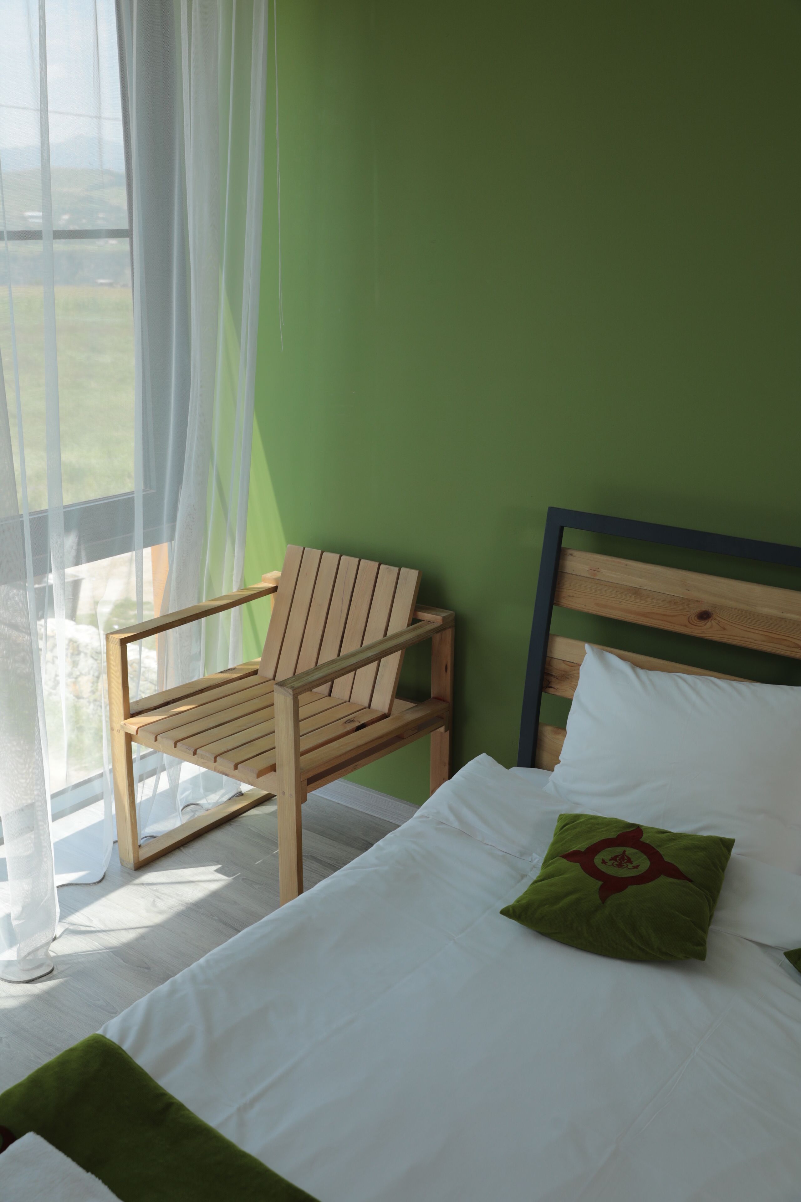 A room with a bed, a wooden chair, and a view through a window.