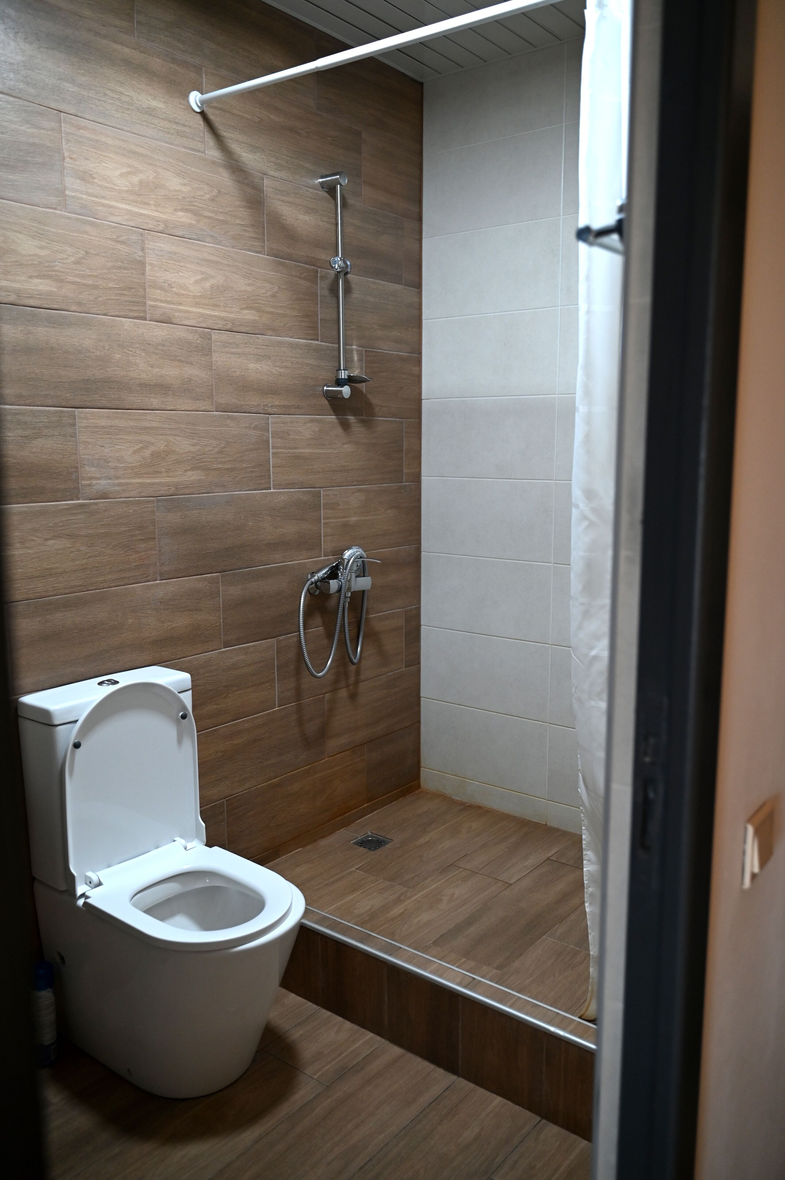A modern bathroom with a wooden floor, a white toilet, and a shower with a handheld showerhead.