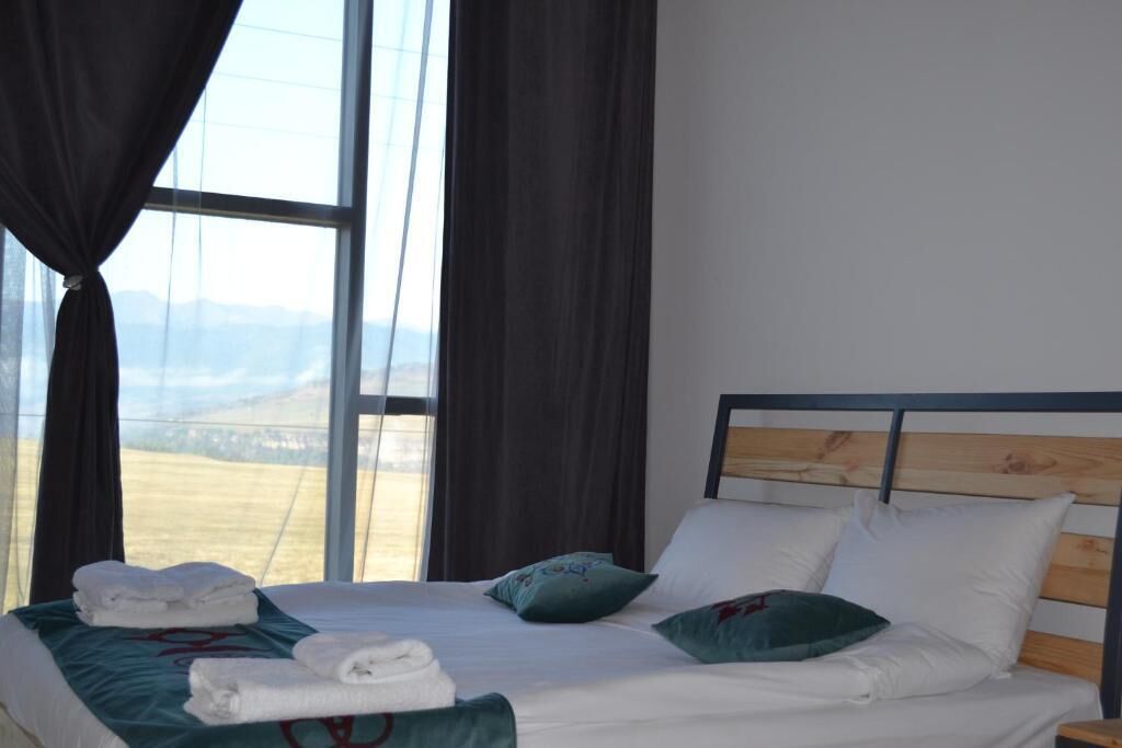 Ein Hotelzimmer mit einem großen Fenster, einem ordentlich bezogenen Bett mit weißer Bettwäsche und Blick auf die Landschaft.