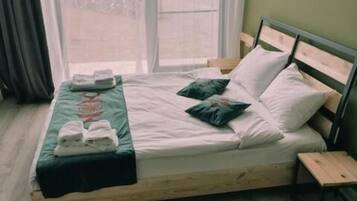 Un lit simple avec un cadre en bois, une literie blanche et un oreiller vert. Une petite table de chevet en bois se trouve à côté du lit.