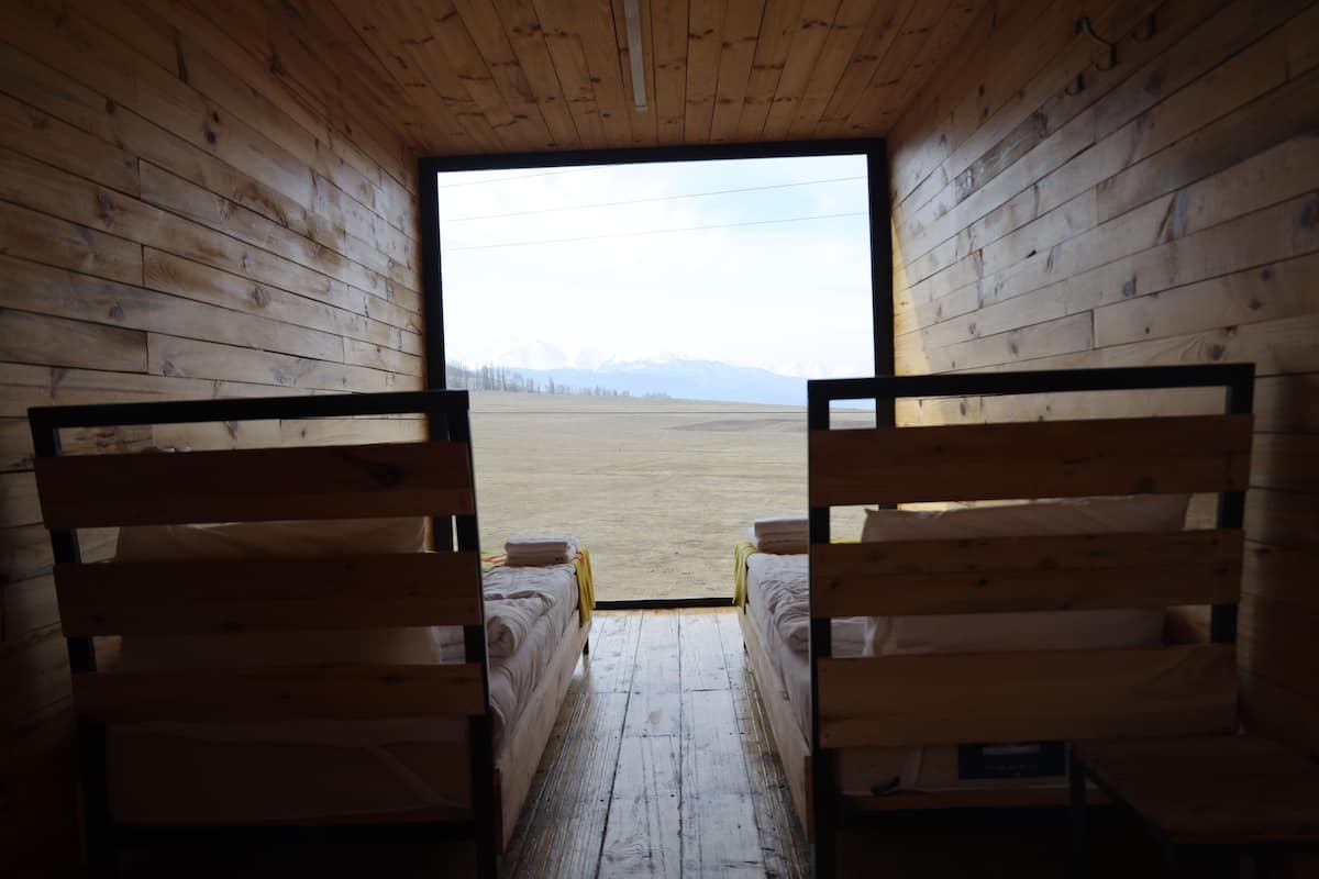 Una cabaña con dos camas de madera frente a un ventanal grande.