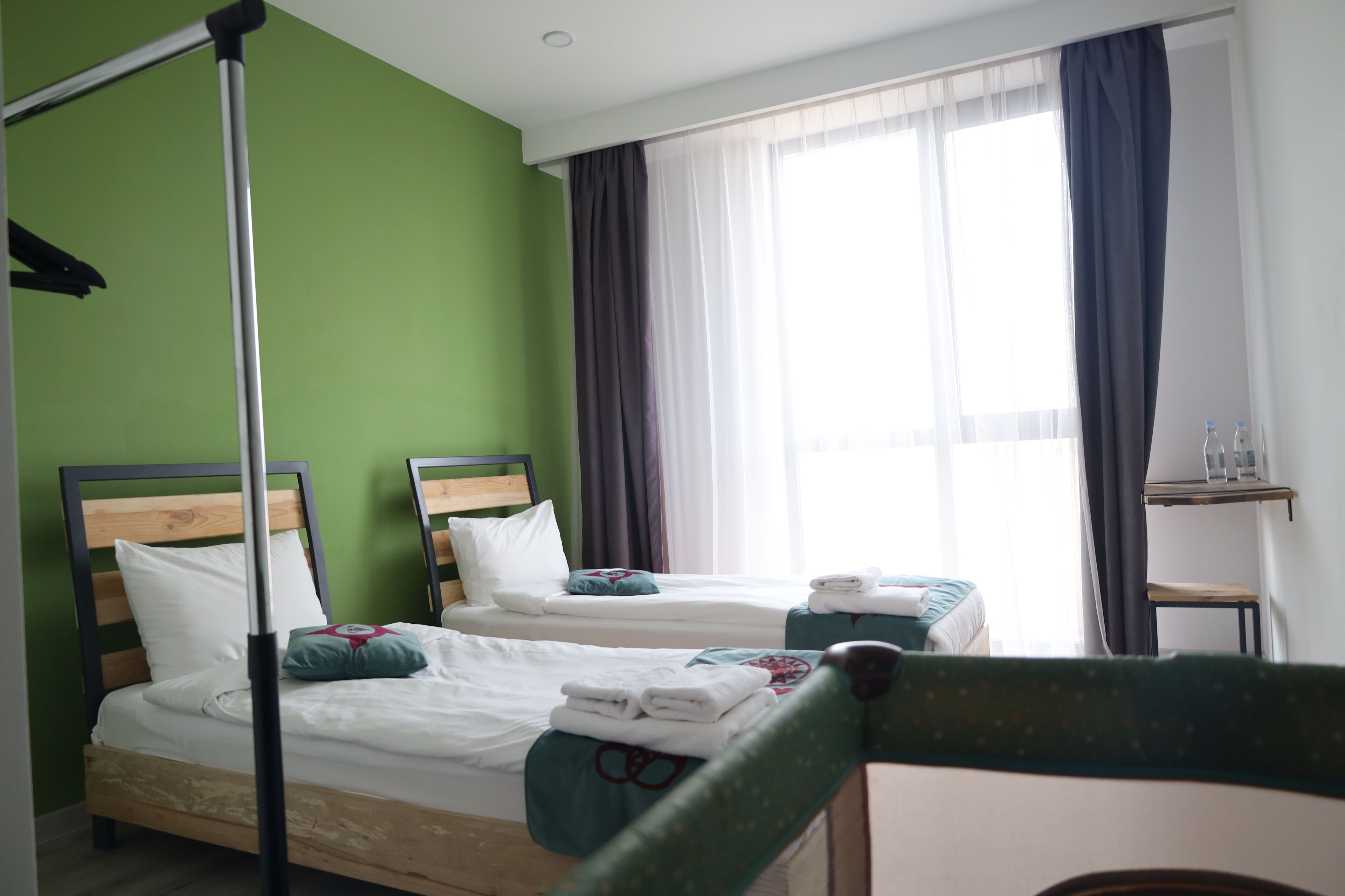 A hotel room with two beds, green walls, a window with curtains, and a small table with toiletries.