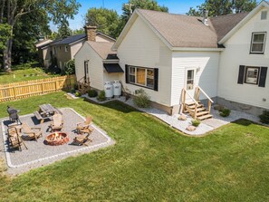 A two-story house with a front yard, a fire pit, outdoor seating, and a staircase leading to the front door.