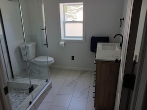 A bathroom with a toilet, shower, sink, and a window. - Salmon River Getaway - Firepit, BBQ & River Views (Richland)