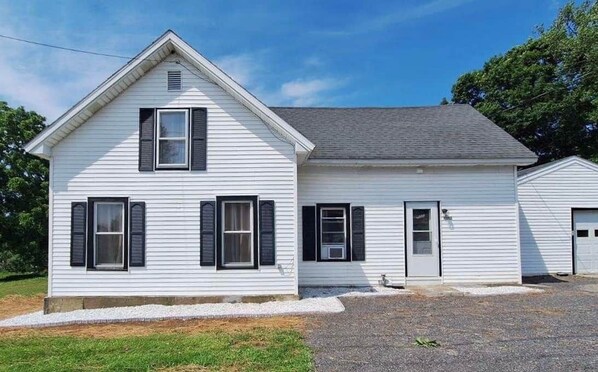 A white single-story house with black shutters, a garage, and a gravel driveway. - Salmon River Getaway - Firepit, BBQ & River Views (Richland)