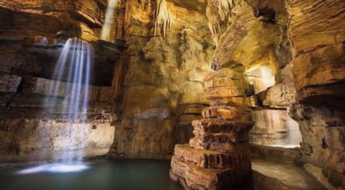 Eine Höhle mit Wasserfall, Felsformationen und einem Wasserbecken.