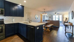A modern kitchen with dark cabinetry, a central island, and a dining area with a bench. - Cozy Condo - Table Rock Lake Community in Hollister, MO (Hollister)