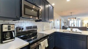 A modern kitchen with dark blue cabinets, a stainless steel microwave, a built-in oven, and a coffee maker. - Cozy Condo - Table Rock Lake Community in Hollister, MO (Hollister)