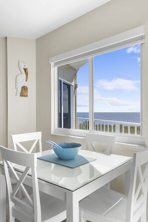 A white dining table with a blue bowl, white chairs, and a view of the ocean through a window. - Amazing Ocean view at Ocean Pointe w/Heated Pool (Tavernier)