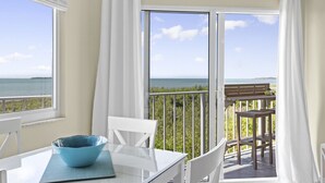 Ein Balkon mit Tisch und Stühlen, Blick aufs Meer, und ein weißer Stuhl mit einer blauen Schüssel auf dem Tisch.