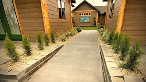 A pathway leading to a row of log cabin-style buildings with a mural on the central building. - Bear Mountain -Suite 4 (Grants Pass)