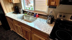 A kitchen with wooden cabinets, a granite countertop, a stainless steel sink, a toaster, and a black stove. - Bear Mountain -Suite 4 (Grants Pass)