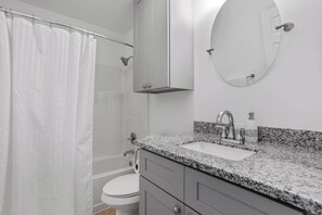 A bathroom with a shower curtain, a toilet, a sink with a granite countertop, and a mirror. - Rest Nest Lounge Cozy Spot for Fun and Calm - HAR3 (Iowa)