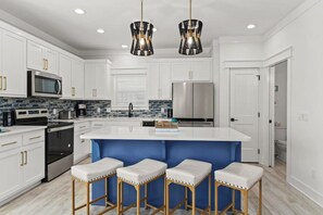 Una cocina moderna con armarios blancos, electrodomésticos de acero inoxidable, una isla azul con taburetes e iluminación colgante.