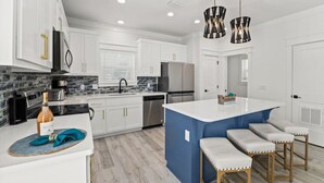 Una cocina moderna con gabinetes blancos, una isla azul, electrodomésticos de acero inoxidable y una barra con taburetes.