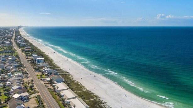Vista aérea de una zona costera con playa, casas y una carretera.