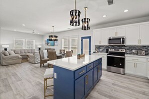 Una cocina moderna con armarios blancos, una isla azul, electrodomésticos de acero inoxidable y un comedor con sofá y sillas.