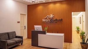 A reception area with a wooden panel wall, a reception desk, a chandelier, a sofa, and potted plants.