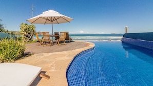 Un espace aménagé au bord de la piscine, avec une terrasse en bois, une table et des chaises, ainsi qu’un parasol.