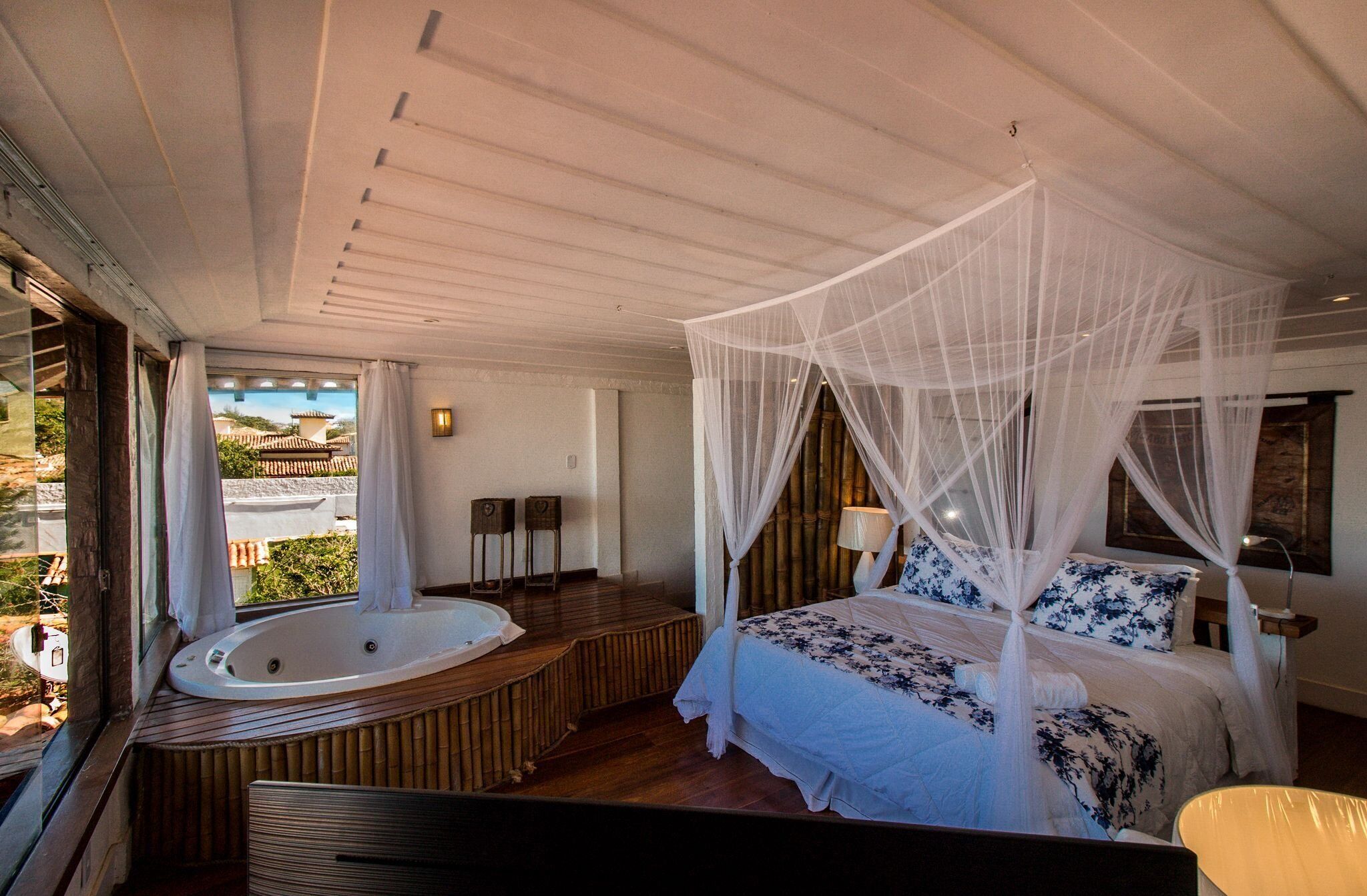 Un dormitorio con cama con dosel, una zona de estar con vistas y un jacuzzi.