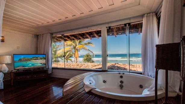 Une pièce dotée d’un plancher en bois, d’une grande fenêtre donnant sur la plage, d’un téléviseur et d’un jacuzzi.