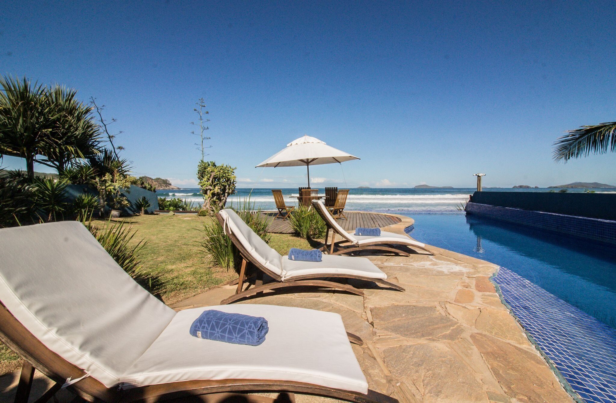 Zona de piscina con sillones reclinables y una sombrilla, con vista al océano.