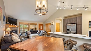 A spacious living room with a fireplace, a large wooden dining table, and a kitchen area with modern appliances. - Walk to the Lifts/Private Garage/Hot Tub Access/Custom Kitchen (Keystone)