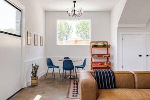 A compact living space with a dining area, a sofa, a chandelier, and a large window.