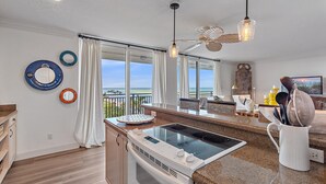 Eine moderne Küche mit einer großen Kochinsel, ein Essbereich mit Blick auf den Strand und ein Balkon mit Meerblick.