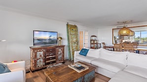 Ein Wohnzimmer mit einem weißen Sofa, einem Holztisch und einem Fernseher auf einem Schrank.
