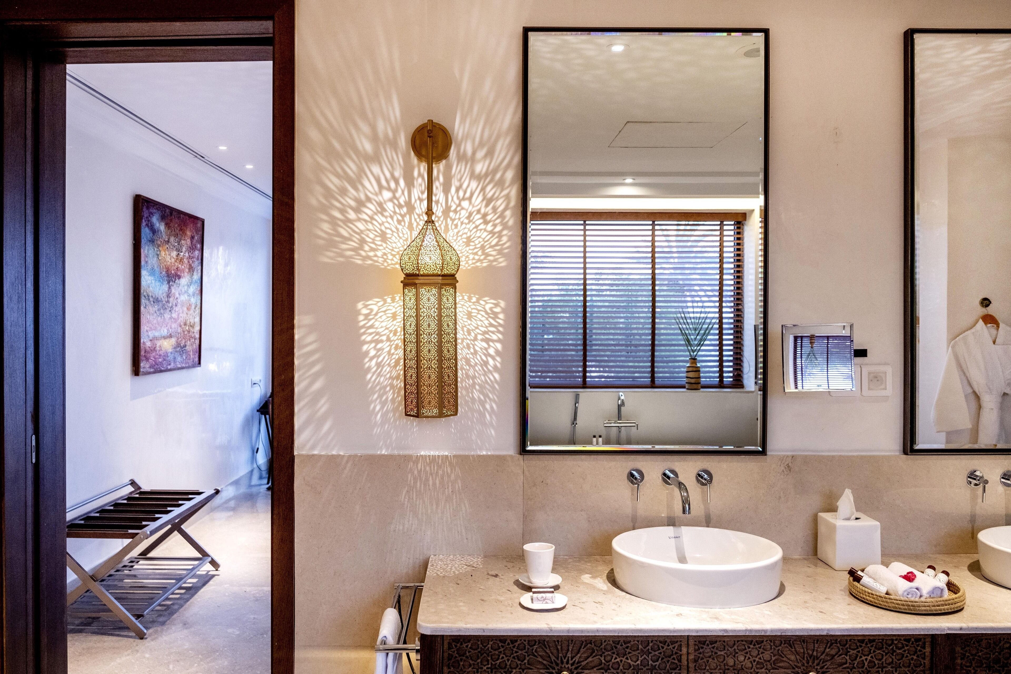 A modern bathroom with a large mirror, two sinks, and a decorative wall light.