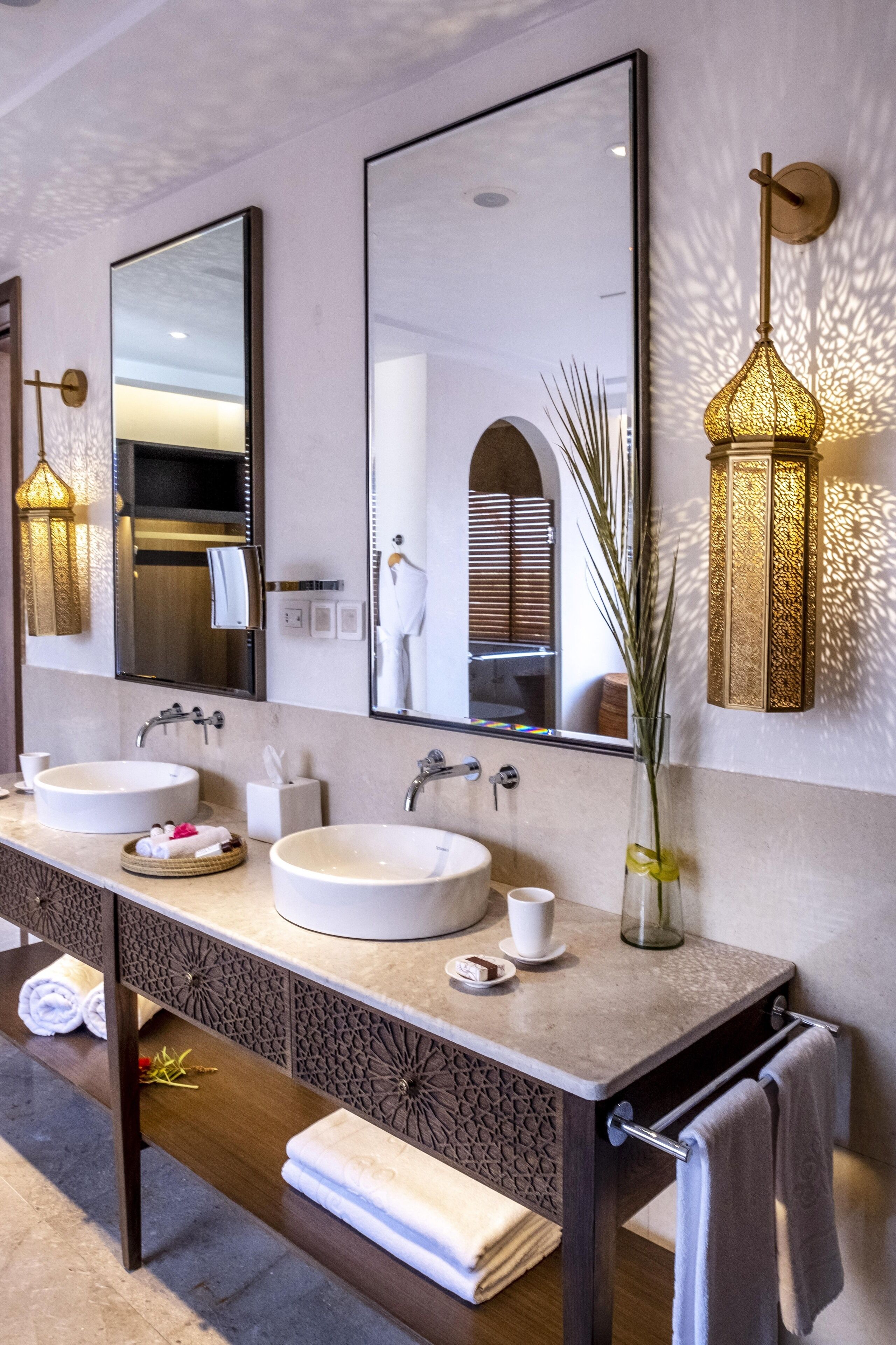 Ein modernes Badezimmer mit zwei Waschbecken, einem großen Spiegel und dekorativen Wandleuchten.