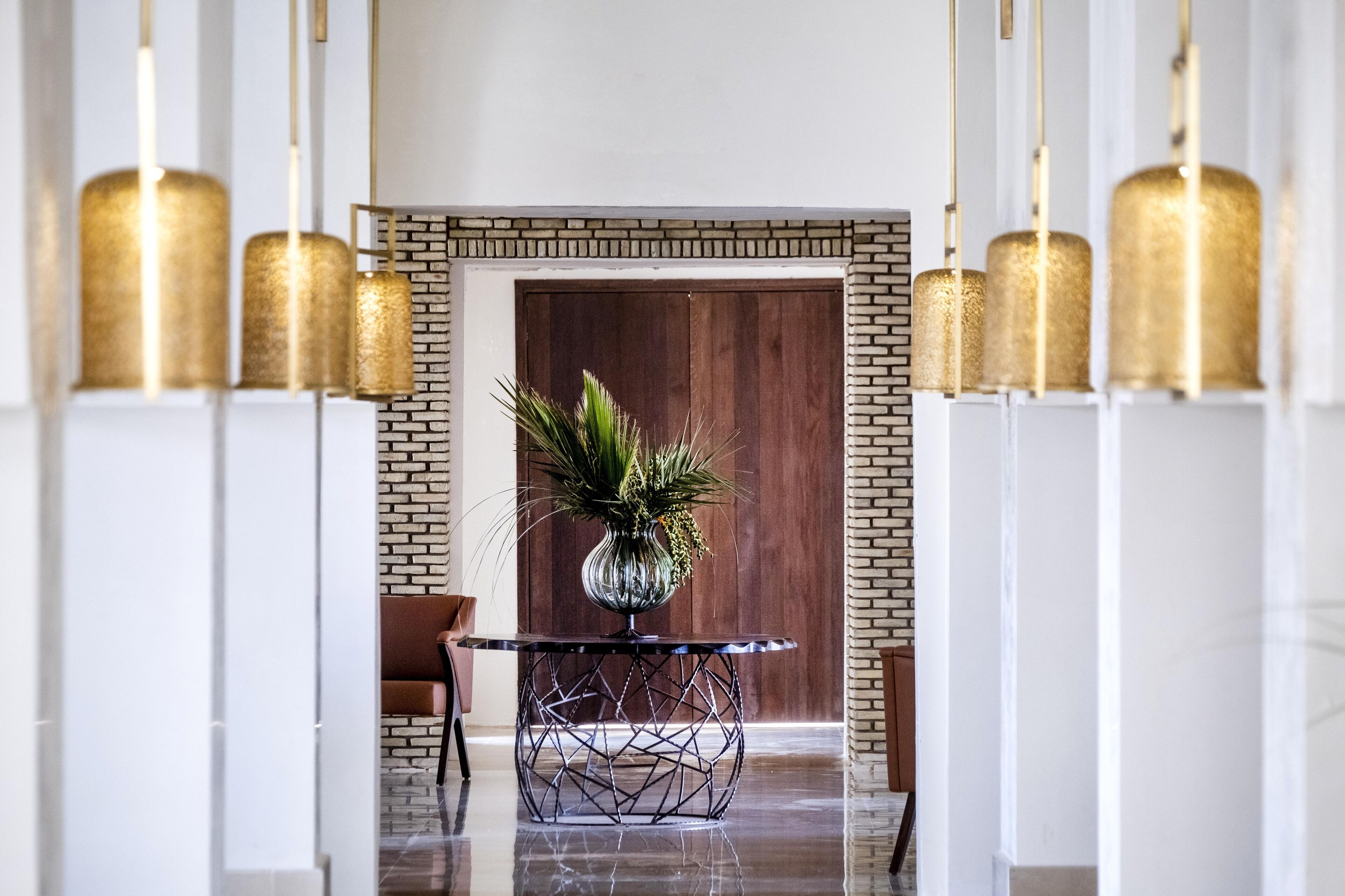 Eine moderne Lobby mit Backsteinwand, einer Holztür und einem runden Tisch mit geometrischem Fuß.