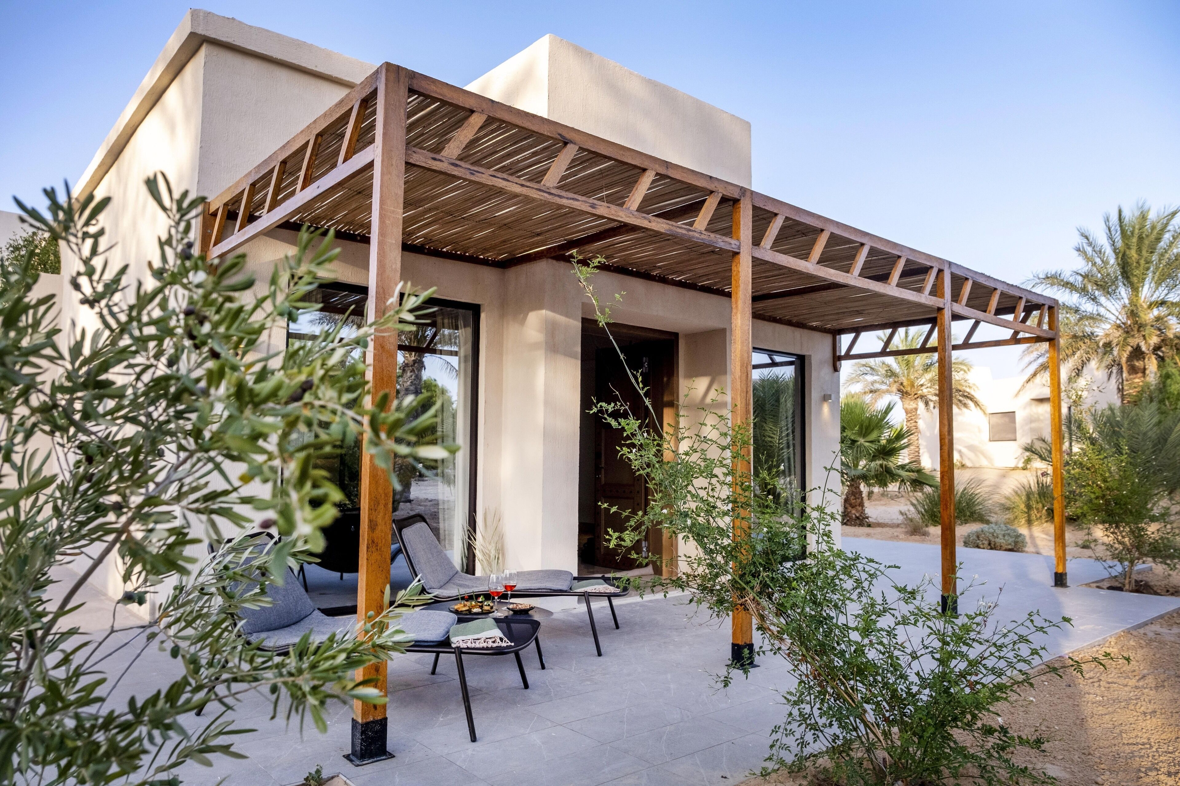 A modern outdoor patio with two lounge chairs, a wooden pergola, and a view of a desert landscape.