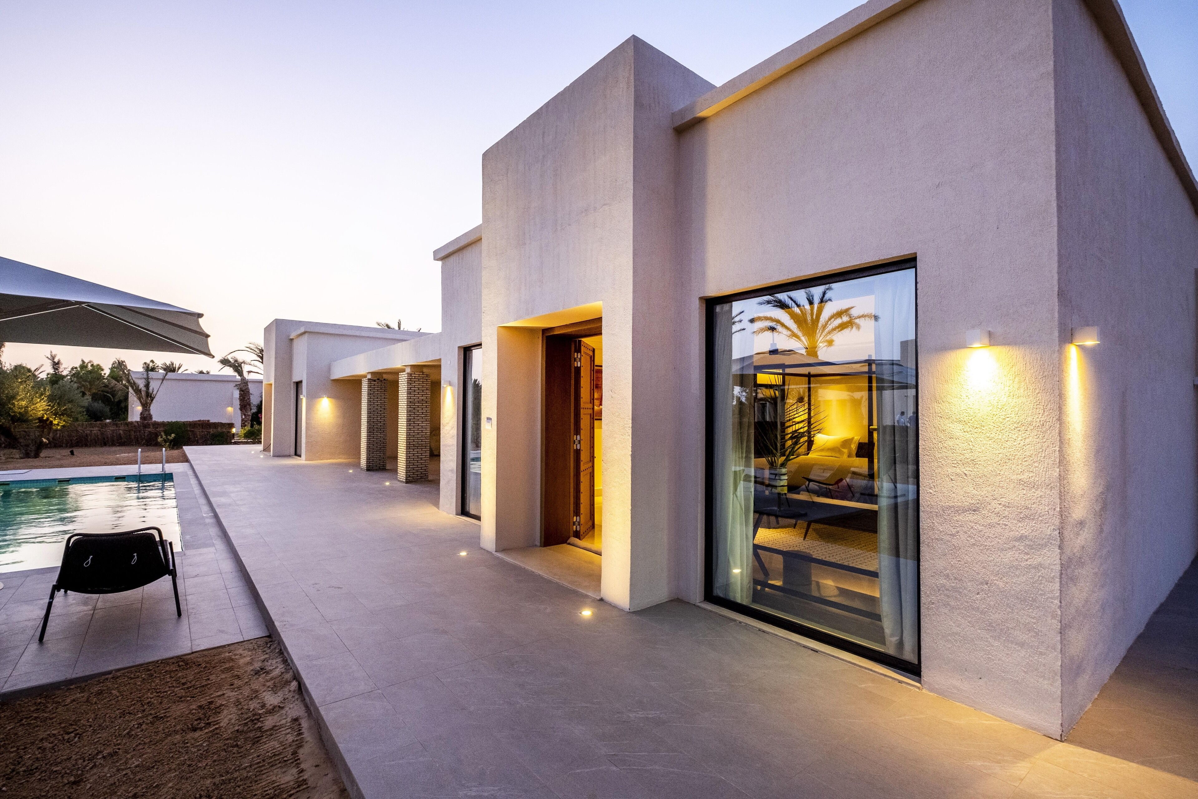 A modern house with a pool, large windows, and a well-lit interior.