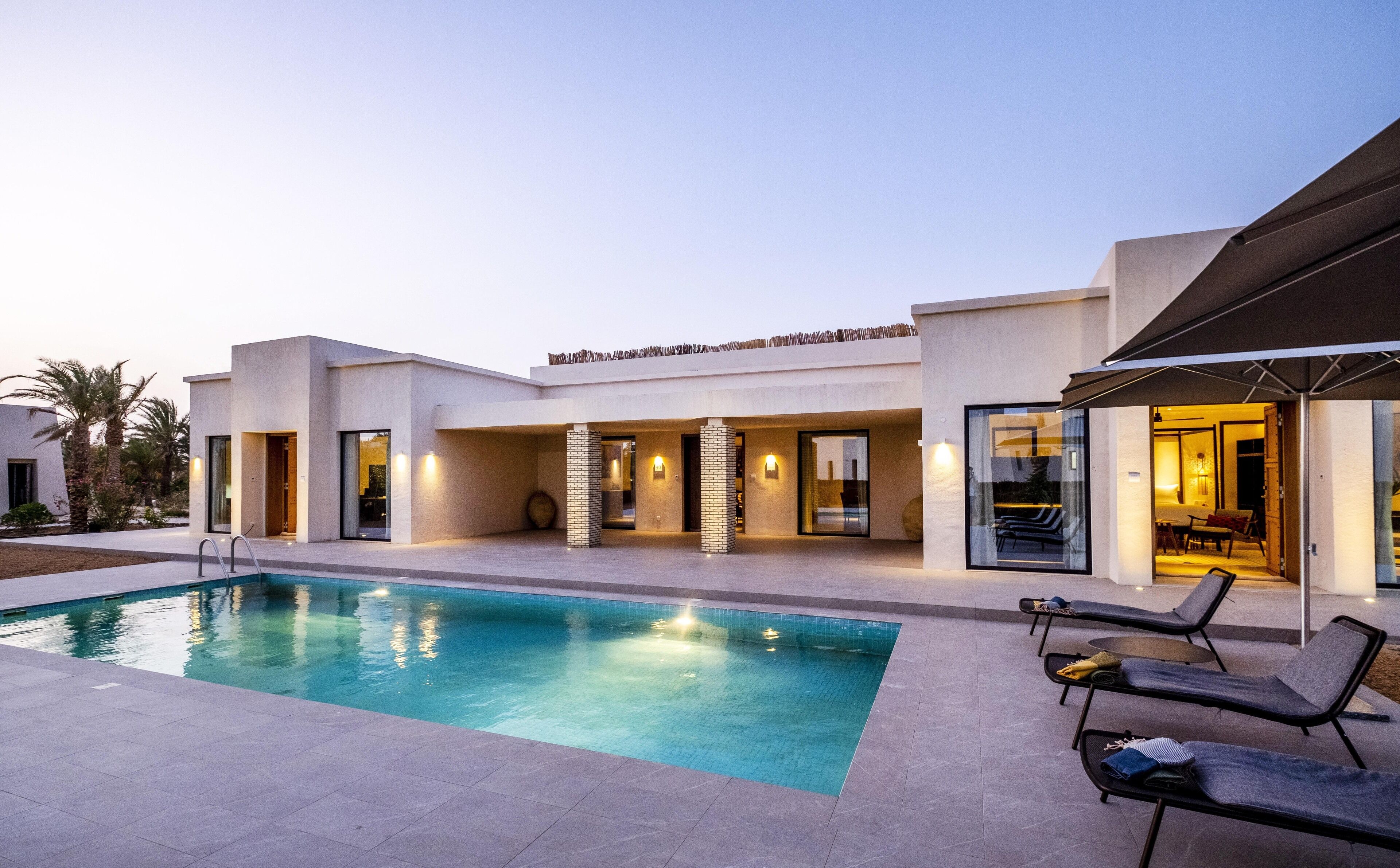 A modern pool area with a clear pool, lounge chairs, and a covered seating area.